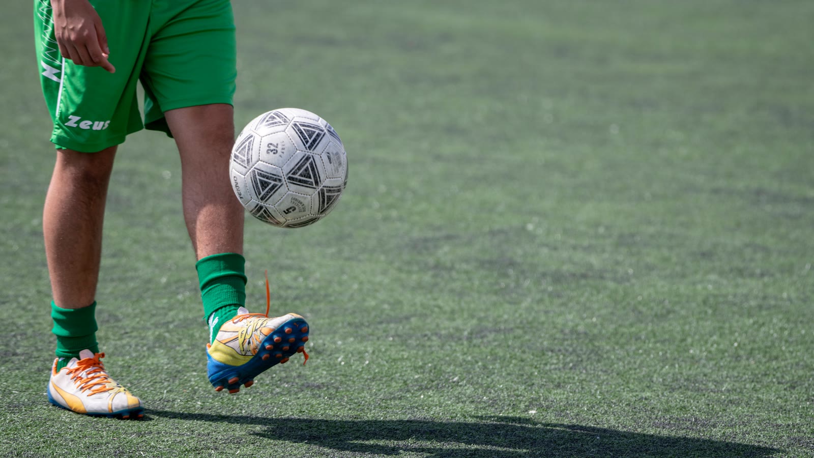 En fodbold balanceret på en spillers fod på græsbanen